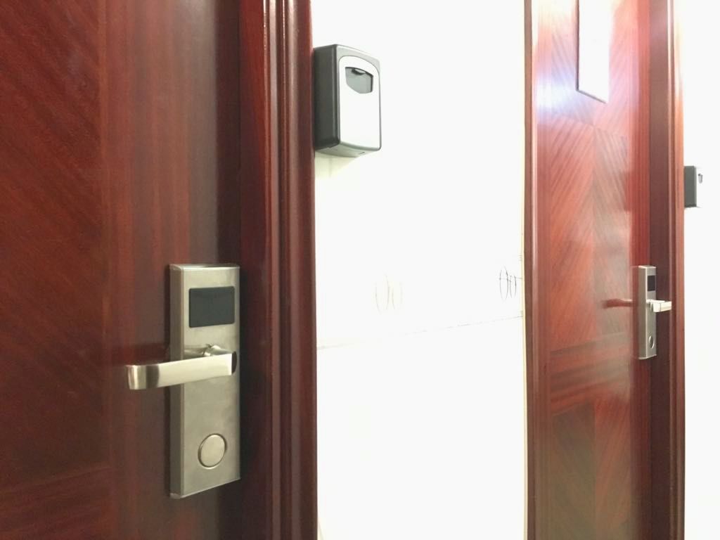 Une porte en bois équipée d’une serrure électronique moderne et d’un petit appareil rectangulaire fixé au mur juste au-dessus.