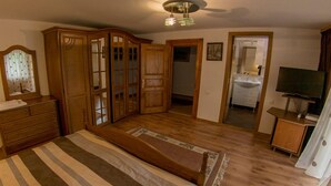 A bedroom with a bed, wooden wardrobe, a mirror, a television, and a bathroom visible through an open door. - Vila Flora Viseu de Jos (Viseu de Jos)