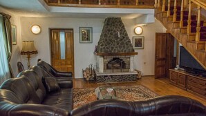 A living room with a stone fireplace, leather sofa, wooden staircase, and a television. - Vila Flora Viseu de Jos (Viseu de Jos)
