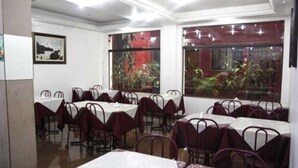 Un restaurante con varias mesas y sillas, amplias ventanas con plantas y obras de arte enmarcadas en las paredes.