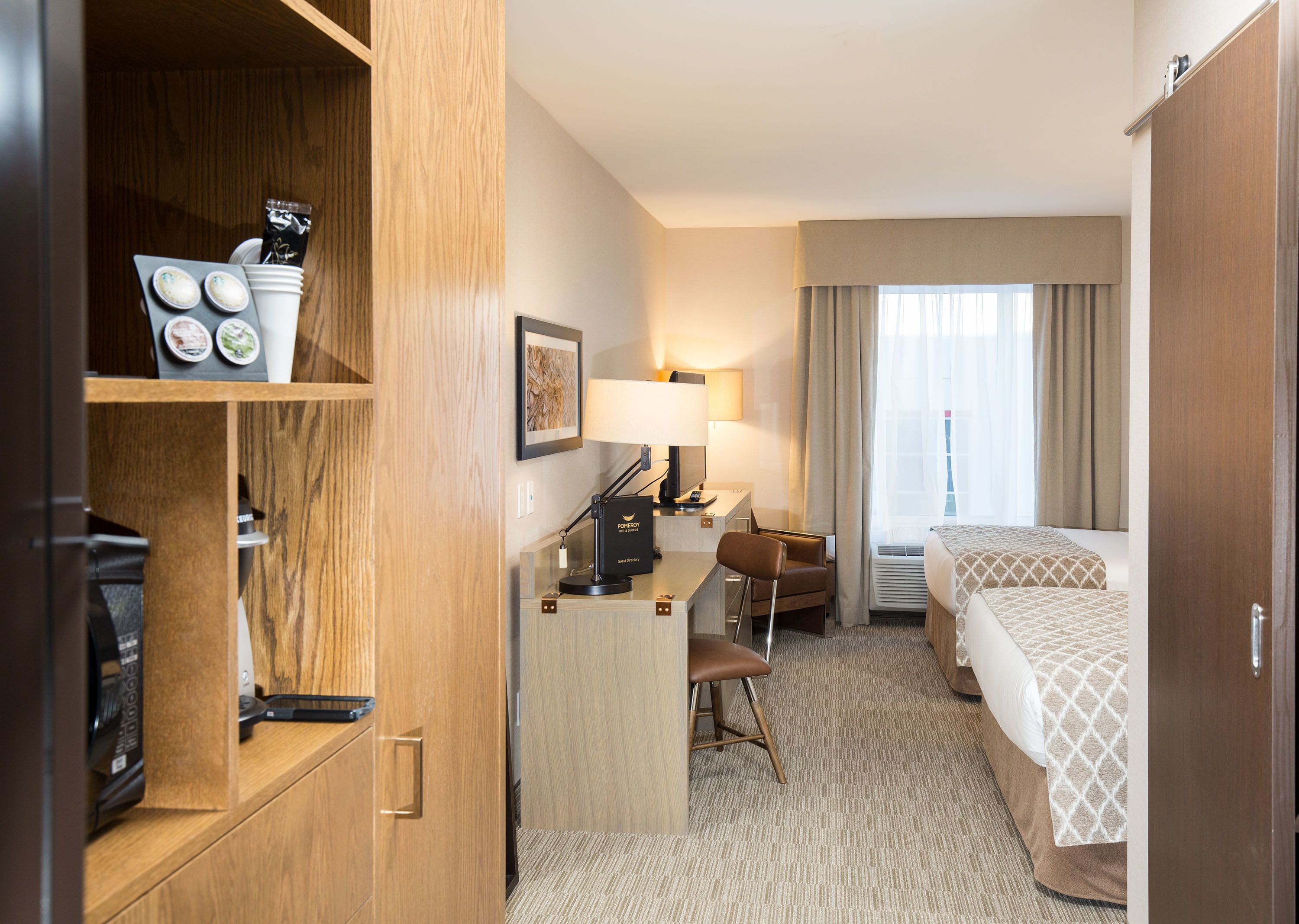 A hotel room with a desk, chair, bed, and a wardrobe.