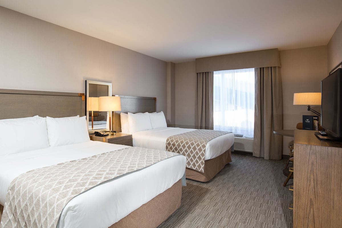 A hotel room with two beds, a TV, a desk, and a window with curtains.