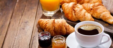 A wooden table with croissants, a glass of orange juice, a cup of coffee, and two small jars of jam.