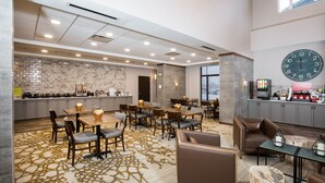 A hotel lobby with a kitchen area, dining tables, chairs, and a large clock on the wall. - Pomeroy Inn & Suites Prince George (Prince George)
