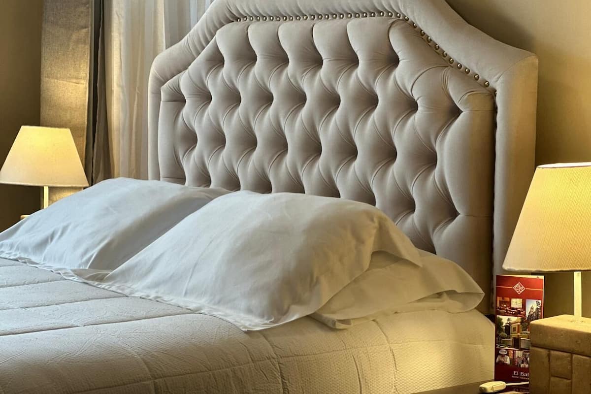 Ein Bett mit einer gepolsterten Kopfteile, weißer Bettwäsche und einem Nachttisch mit einer Lampe.