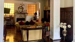 Amplia sala de estar con techo alto, columnas blancas ornamentadas, chimenea y sofá con cojines.
