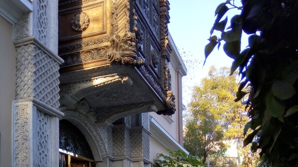 Un edificio con detalles arquitectónicos ornamentados, incluyendo una entrada decorativa y un balcón con intrincados trabajos de metal.