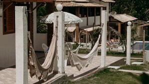 Un hamac installé dans une cour avec une piscine, et en arrière-plan, une structure dotée d’un toit de chaume.
