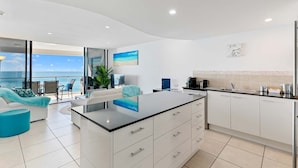 A modern kitchen with white cabinets, a black countertop, and a view of the ocean.