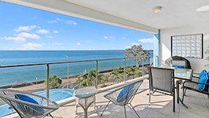 A balcony with a view of the ocean, a pool, and outdoor furniture.