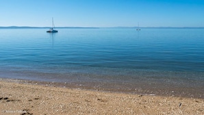 A calm beach with a clear sky and a sailboat in the distance.