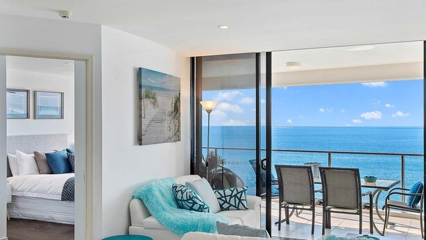 A balcony with a view of the ocean, a sofa, a chair, and a small table.