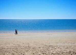 A beach with a person walking on the sand.