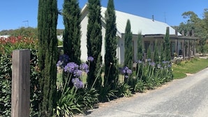 Ein Gebäude mit weißem Dach und einem Garten mit hohen Bäumen und violetten Blüten.