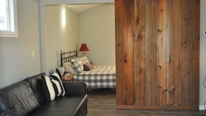 A bedroom with a bed, a red lamp, a black and white checkered bedspread, a black leather sofa, and a wooden sliding door. - New Loft w/South River view from treehouse deck! (Riva)
