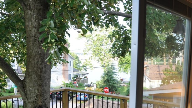 A wooden deck with a glass door, a tree, and a stop sign in the background. - New Loft w/South River view from treehouse deck! (Riva)
