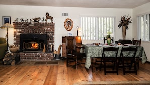 Un salon chaleureux avec une cheminée en briques, un plancher en bois et un coin repas avec une table dressée pour quatre personnes.