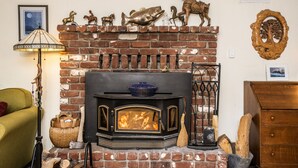Un salon chaleureux avec une cheminée en briques, un fauteuil vert et des statues de chevaux décoratives.