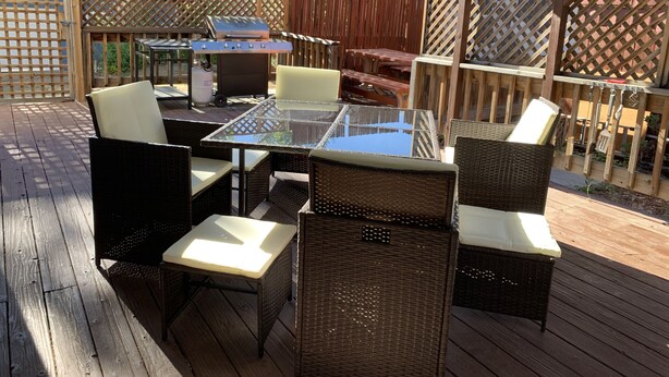 Une terrasse extérieure aménagée avec des meubles en osier, une table à plateau en verre et un barbecue.