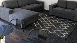 A modern living room with two grey sofas, a wooden dining table, and a patterned rug.