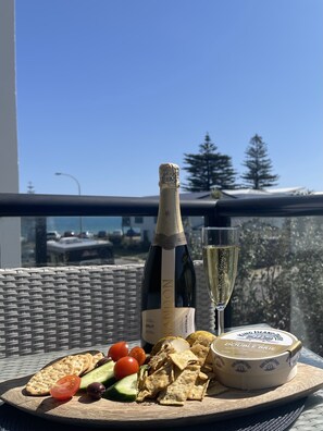 A table with a bottle of Brut wine, a glass of wine, crackers, cheese, and olives on a balcony overlooking a cityscape.