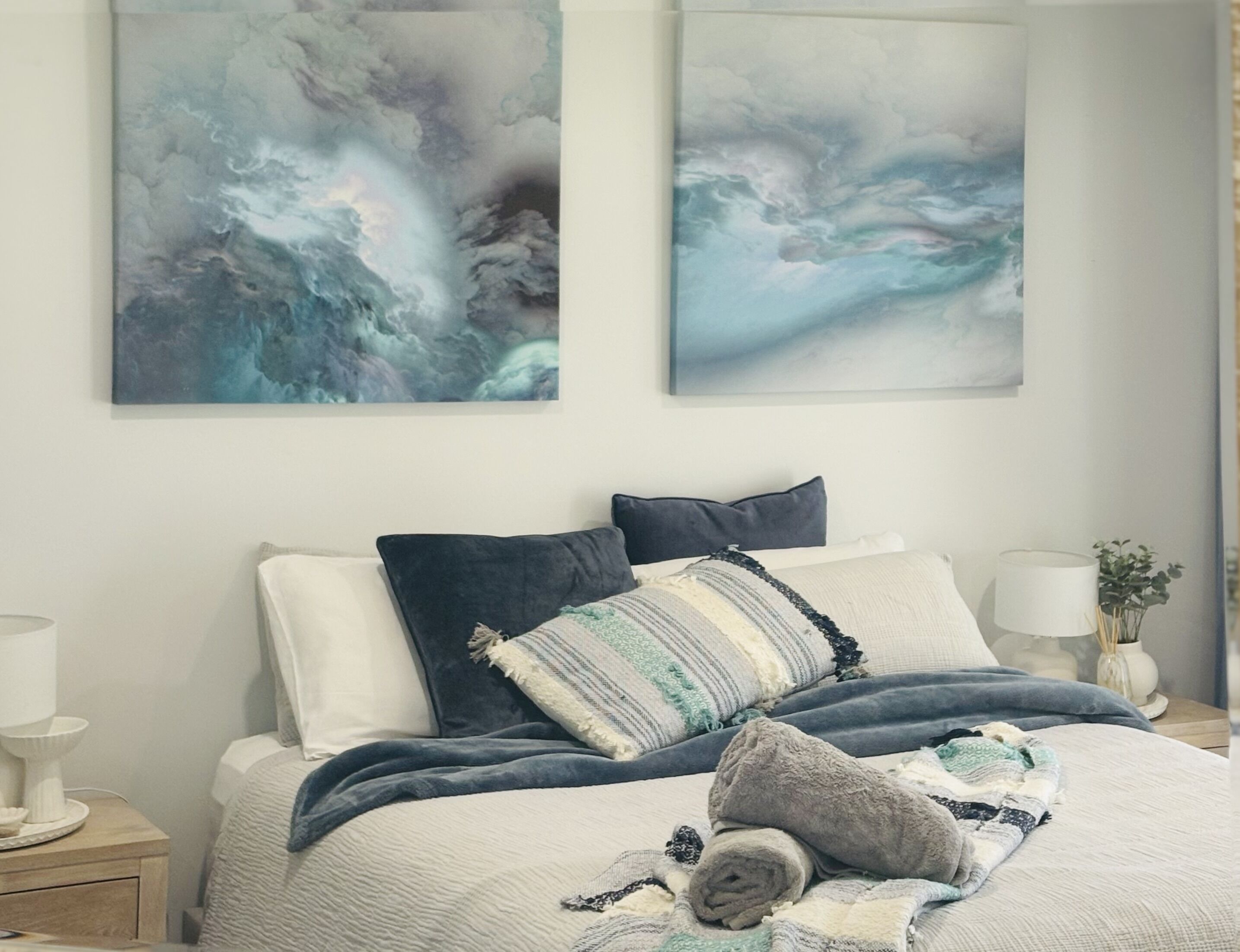 A bedroom with a bed, pillows, a bedside table, and wall art.