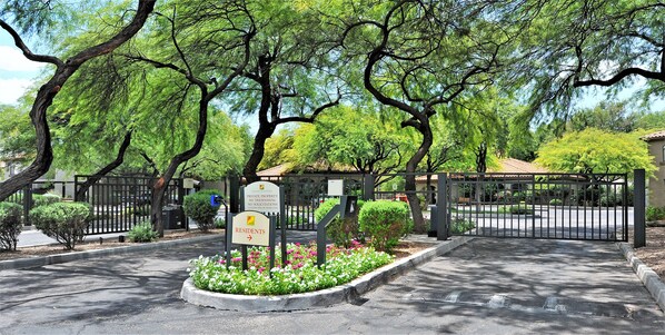 gated community with a pathway leading to a building surrounded by mature trees and well-manicured landscaping.