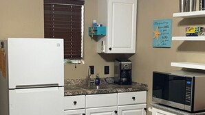 Una cucina compatta con mobili bianchi, un frigorifero, un forno a microonde e una macchina per il caffè.