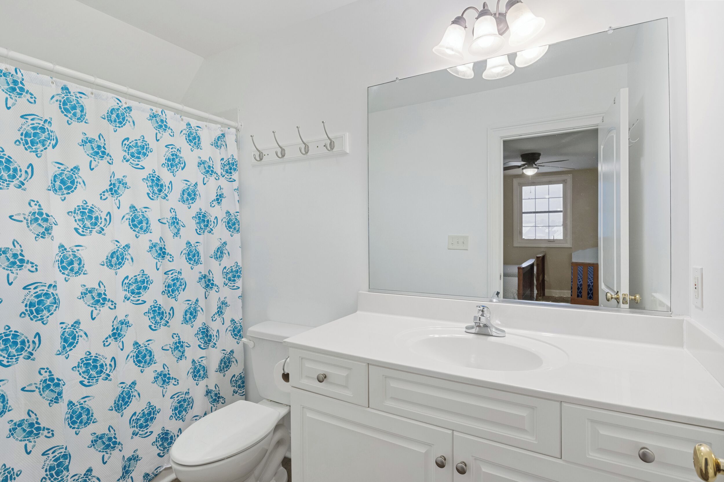 A bathroom with a white sink, vanity, and toilet. There is a shower curtain with a blue sea turtle pattern.