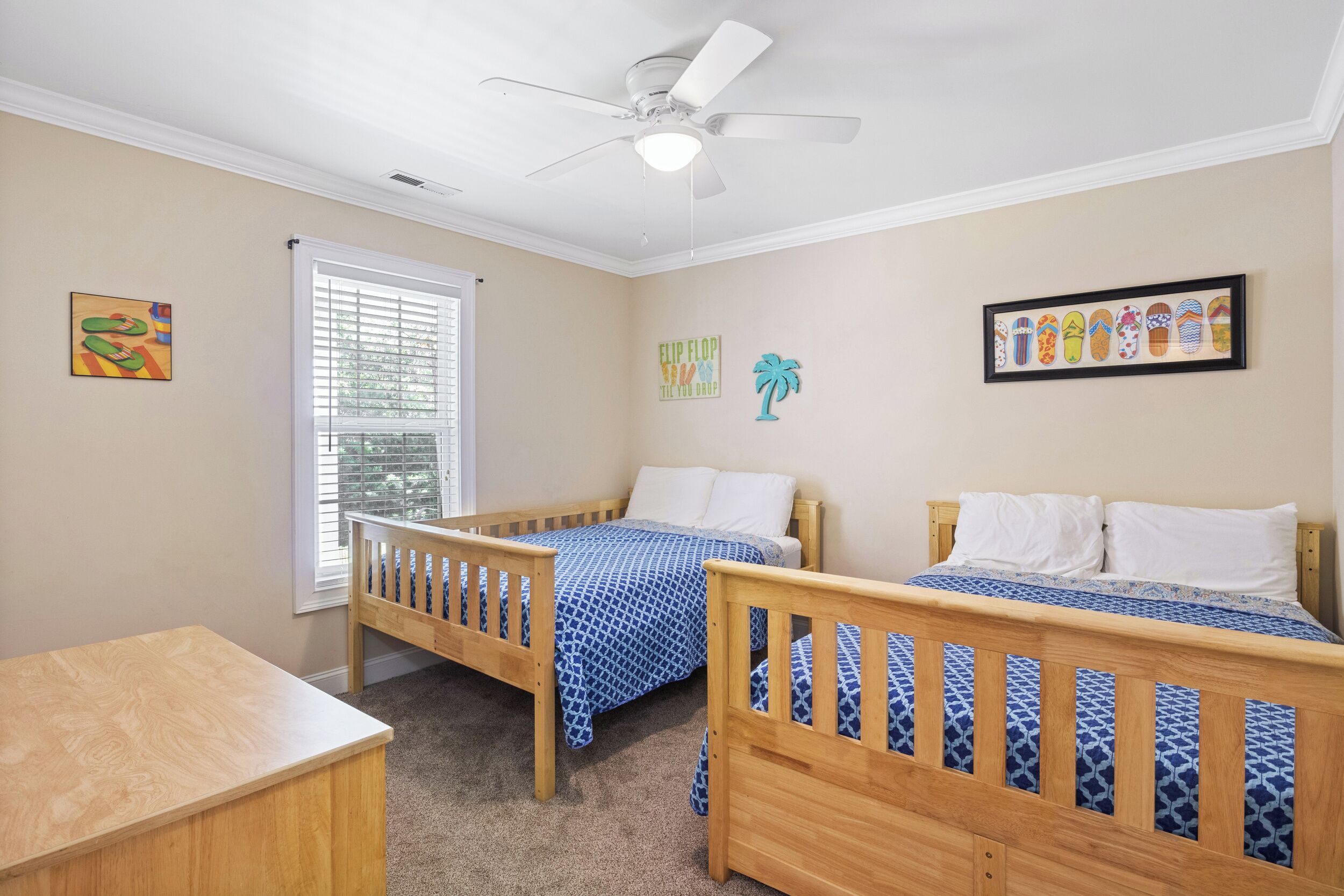 A bedroom with two single beds, a ceiling fan, a window with blinds, and a framed picture of flip-flops on the wall.