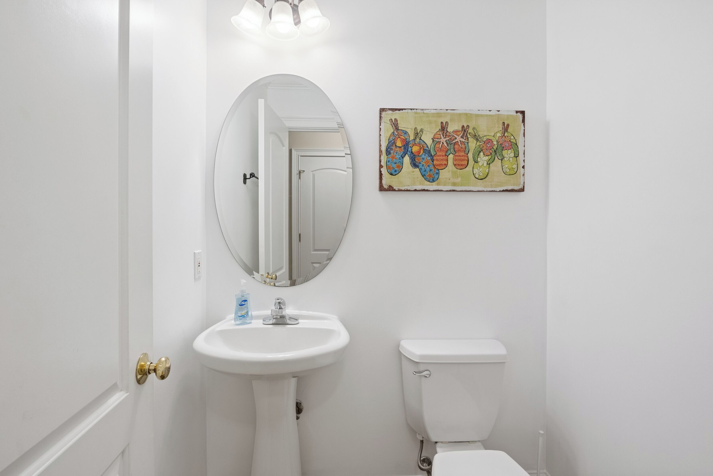 Et badeværelse med et hvidt håndvask, toilet og spejl.