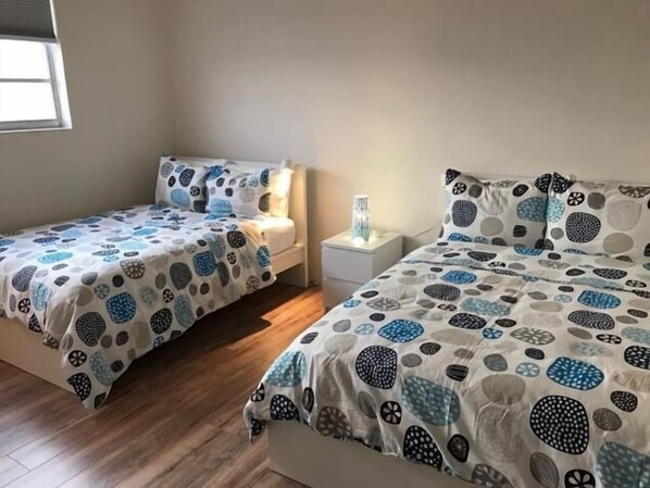 A bedroom with two beds, each with a patterned bedspread and matching pillows. There is a bedside table with a lamp between the beds. - F- Beautiful view of pool and gardens! Walk to beach! (Sunny Isles Beach)