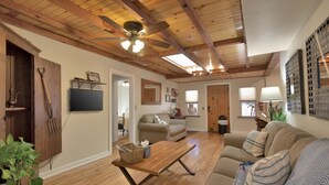 A spacious living room with wooden floors, a ceiling fan, a sofa, a coffee table, and a television mounted on the wall. - The Barn house - 1.5 miles to Whiskey Row (Prescott)