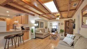 A spacious living area with a wooden ceiling, a sofa, a coffee table, and a kitchen area with wooden cabinets and a refrigerator. - The Barn house - 1.5 miles to Whiskey Row (Prescott)