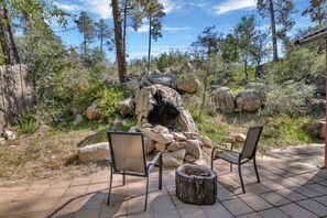 An outdoor patio with two chairs and a wooden stump table, surrounded by rocks and trees.