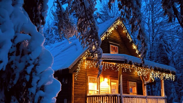 Una baita innevata con facciata in legno, un portico con ringhiere e luci decorative.