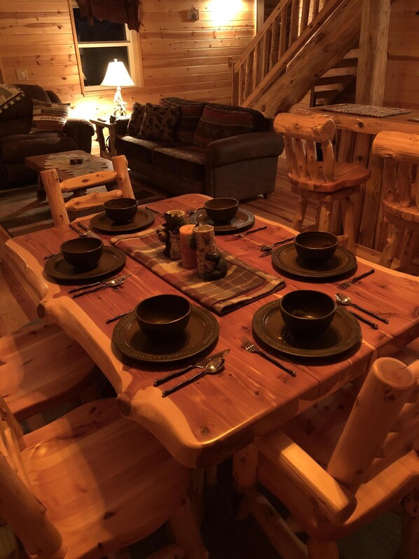 A wooden dining table set with black bowls, plates, and cutlery, surrounded by wooden chairs in a cozy cabin interior. - Cozy, Secluded, Year-Round Cabin: With A Hot Tub! (Munising)
