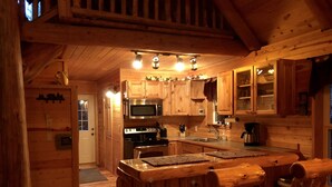 Interno di una baita in legno con angolo cottura, caratterizzato da mobili in legno, un forno a microonde, un fornello e un tavolo da pranzo con sedie.