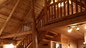 Interno di una baita in legno con angolo cottura, sedie in legno e una scala.