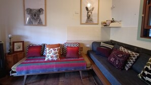 Un salon chaleureux avec un canapé et un banc, des tableaux encadrés au mur et une petite étagère ornée d’objets décoratifs.