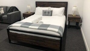 A neatly made bed with a checkered blanket, two bedside tables with lamps, a grey armchair, and a wall-mounted picture.
