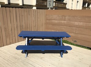 Une table de pique-nique bleue avec un banc, installée sur une terrasse en bois.