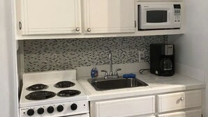 A compact kitchen with white cabinets, a microwave, a stove, and a sink.