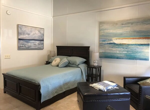 Une chambre à coucher avec un lit, une table de chevet, une chaise et un tableau représentant un bateau accroché au mur.