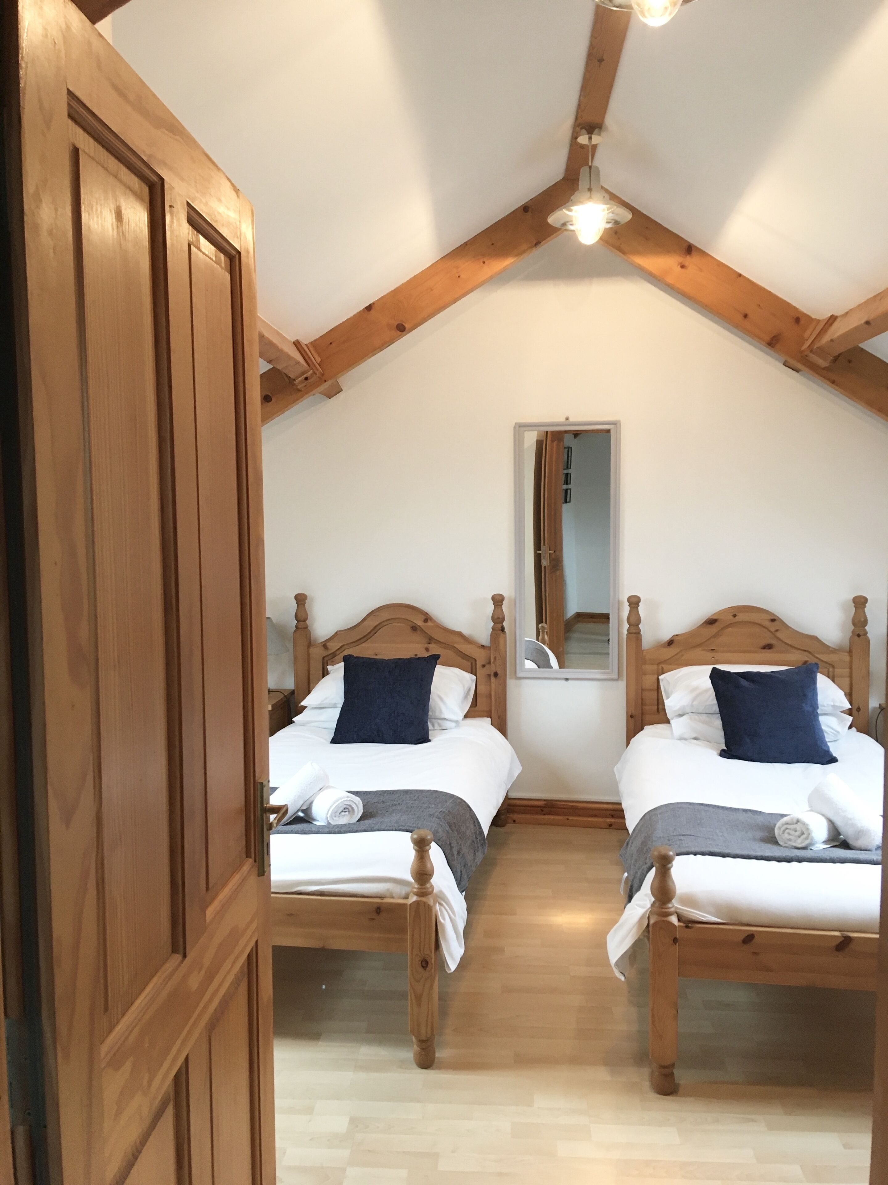 A bedroom with two wooden beds, a wooden wardrobe, and a mirror on the wall.