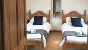 Een slaapkamer met twee houten bedden, een houten kledingkast en een spiegel aan de muur.