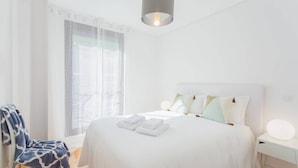 Ein ordentlich eingerichtetes Schlafzimmer mit einem großen Bett, einem Sessel mit Decke und einem Nachttisch mit Lampe.
