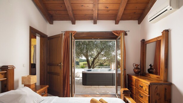 A bedroom with a bed, wooden dresser, and a large mirror. There is a window with curtains, and a hot tub is visible outside. - LUX CASA HISTRIA I - with heated swimming pool & jacuzzi (Pazin)