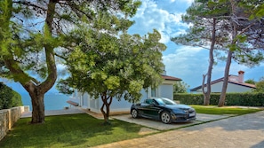 Una casa con entrada de vehículos, un coche aparcado y vista al mar.