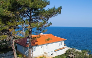 Una casa costera con techo rojo, paredes blancas y vista al mar.